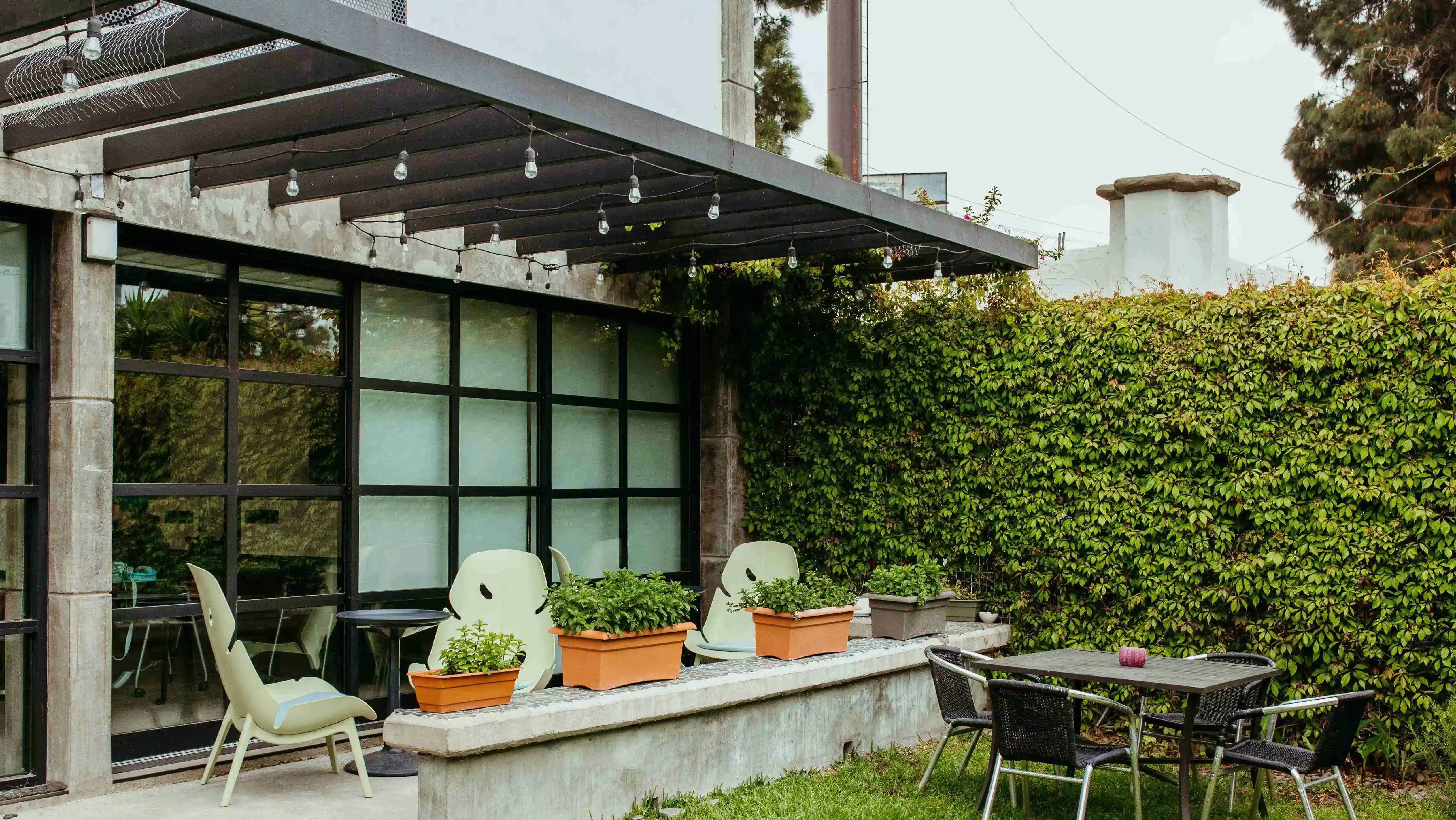  patio trasero con una pérgola, una mesa y sillas de madera, árboles, plantas y una piscina.