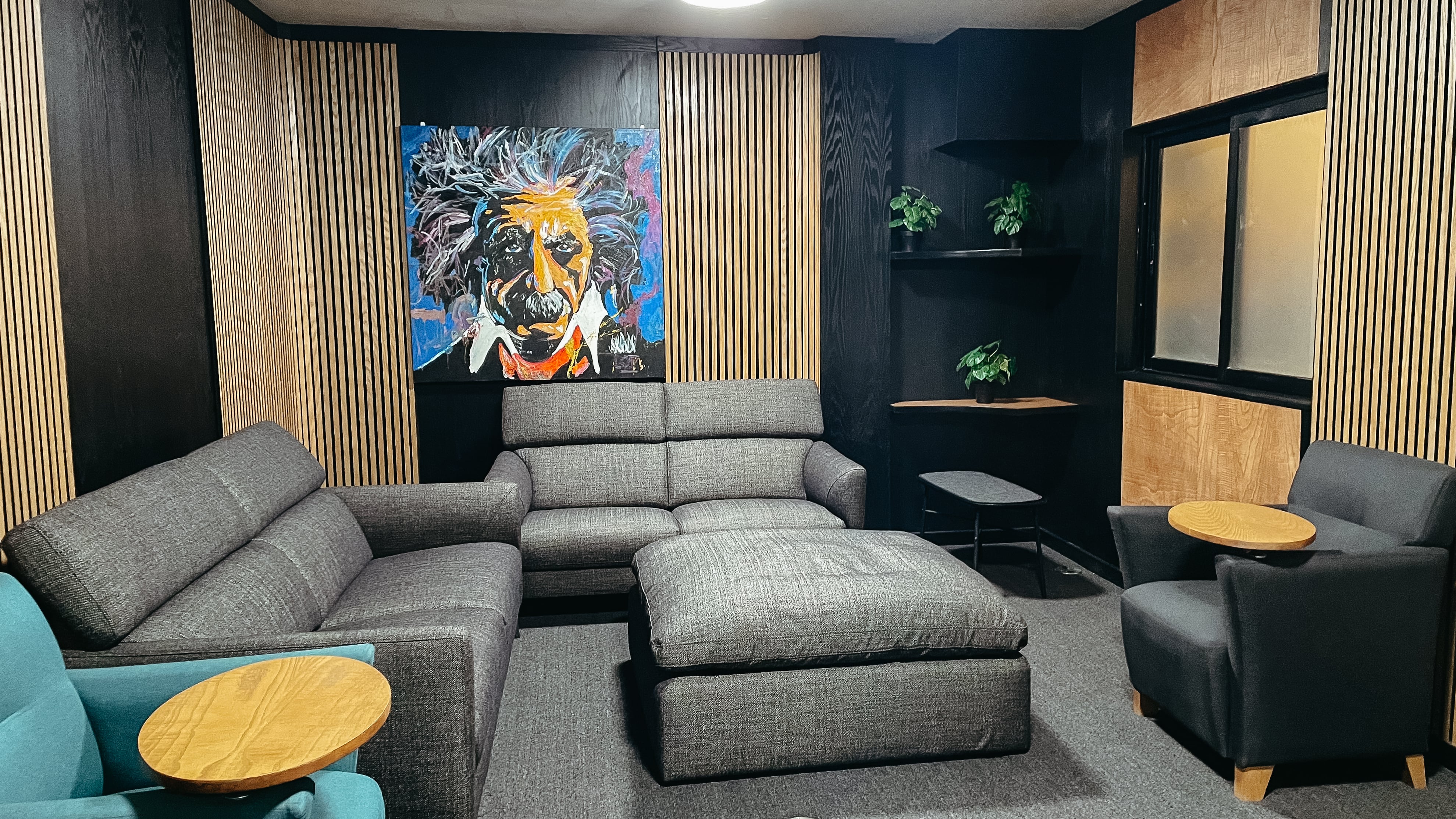 Sala de estar moderna con sofás grises, una pintura colorida de Albert Einstein en la pared, y mesas auxiliares de madera.