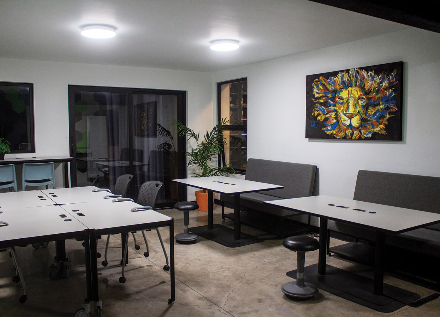 Espacio de trabajo colaborativo con mesas blancas, sillas ergonómicas y una gran pantalla en la pared.